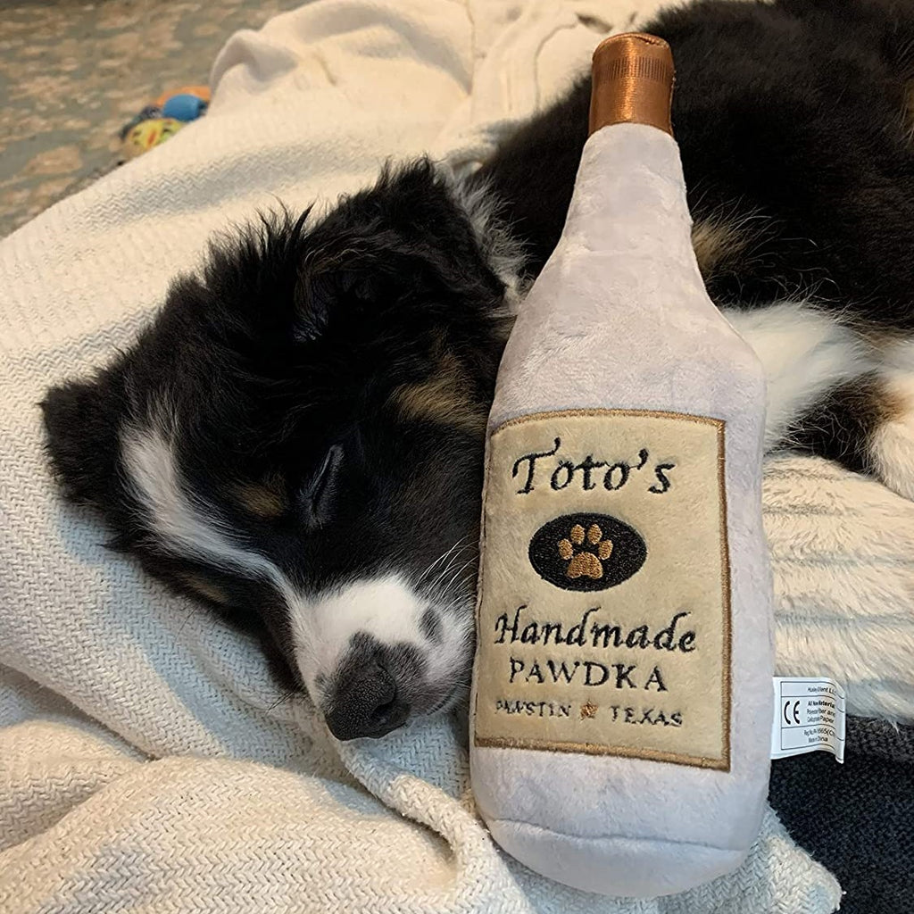 Black and white dog sleeping with Toto's Handmade Pawdka stuffed toy.